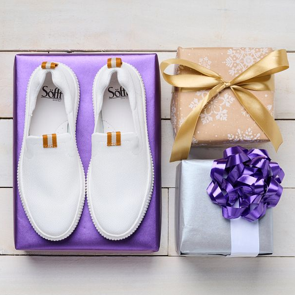 Featuring the Frayda sneaker in white on a purple gift wrapped box.